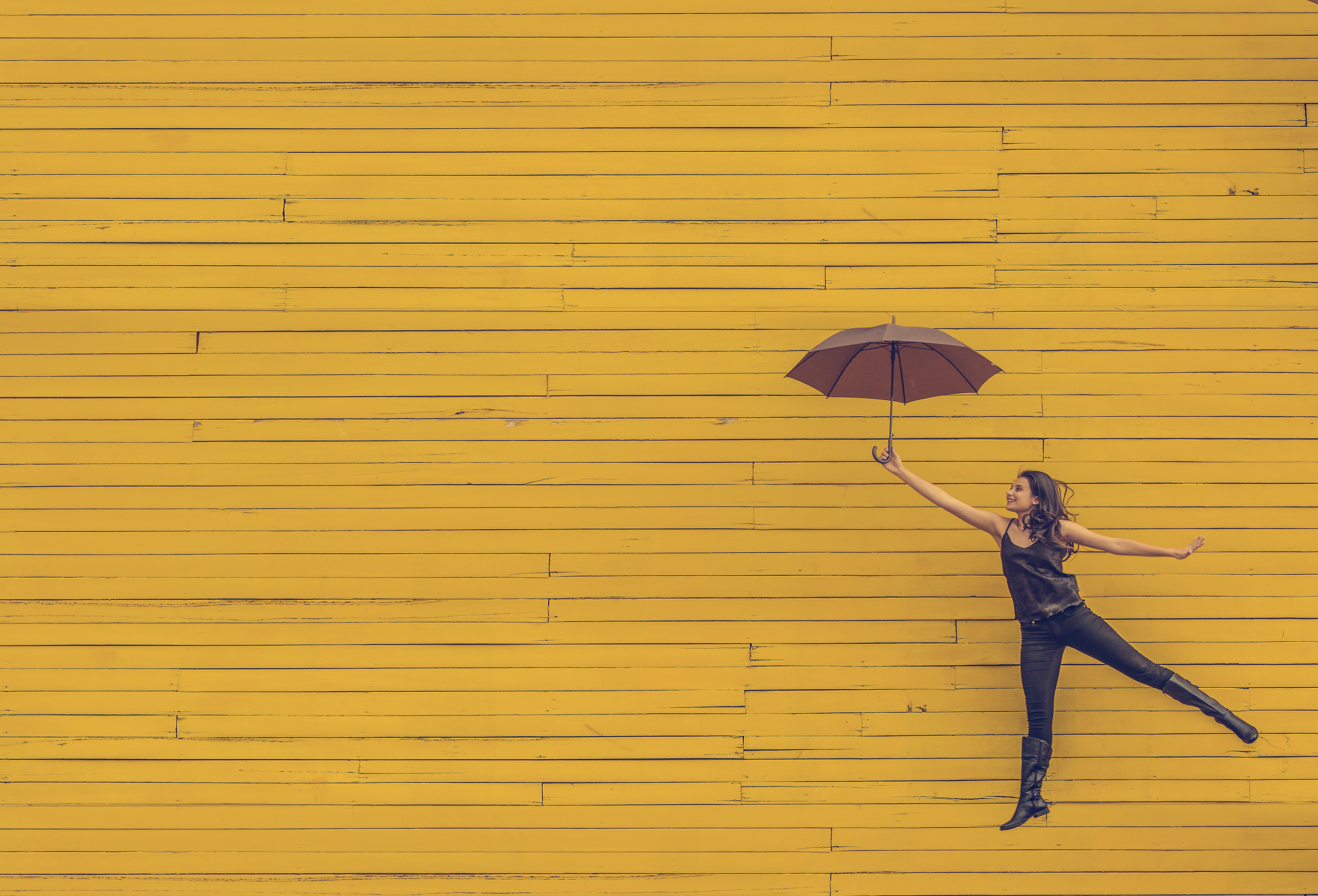 Woman holding an umbrella against a yellow wall