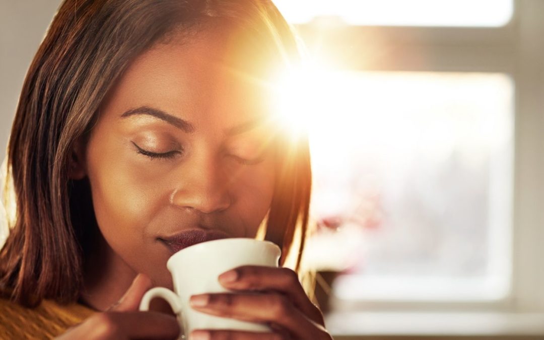 woman drinking coffee while the sun comes up with her eyes closed representing being present