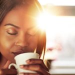 woman drinking coffee while the sun comes up with her eyes closed representing being present